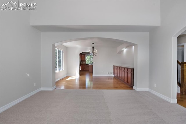 7436 Centennial Glen Dr, Colorado Springs, CO 80919 - unfurnished room featuring light wood-style floors, baseboards, light colored carpet, a chandelier, and arched walkways