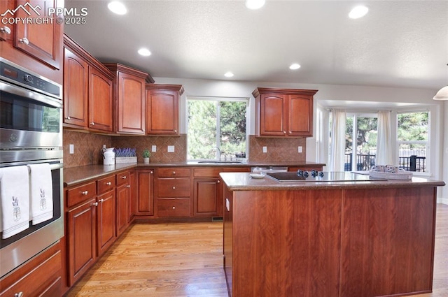 7436 Centennial Glen Dr, Colorado Springs, CO 80919 - kitchen with stainless steel double oven, a sink, light wood-style floors, black electric cooktop, and a kitchen island