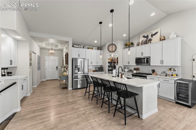kitchen with beverage cooler, a breakfast bar, appliances with stainless steel finishes, light countertops, and light wood-type flooring
