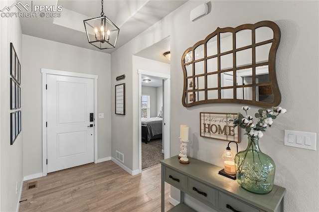 foyer entrance with baseboards, visible vents, an inviting chandelier, and light wood finished floors
