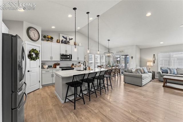 kitchen featuring a breakfast bar, white cabinetry, light countertops, appliances with stainless steel finishes, and open floor plan
