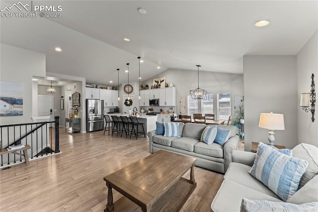 living room featuring lofted ceiling, recessed lighting, light wood finished floors, and a notable chandelier
