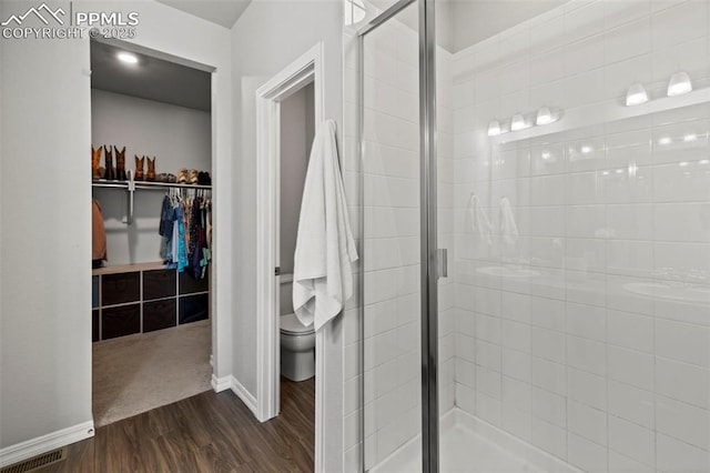 full bath featuring a shower stall, toilet, wood finished floors, and a spacious closet