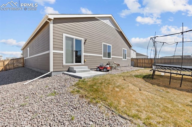 back of property with a yard, a trampoline, and a fenced backyard