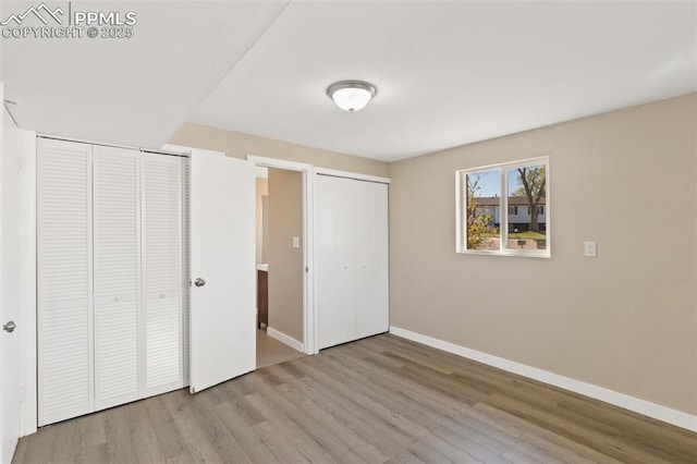 unfurnished bedroom with wood finished floors, multiple closets, and baseboards