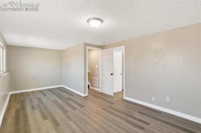 spare room with a textured ceiling, wood finished floors, visible vents, and baseboards