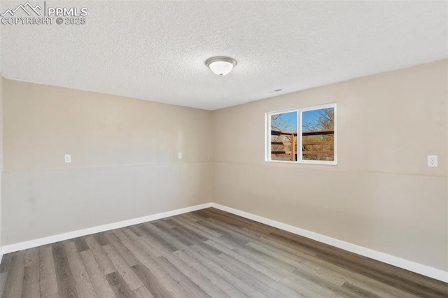 spare room with baseboards, wood finished floors, and a textured ceiling
