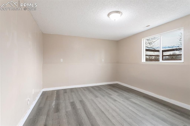 spare room featuring wood finished floors, a textured ceiling, and baseboards
