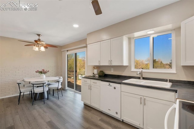 kitchen with dark countertops, white dishwasher, a sink, and ceiling fan