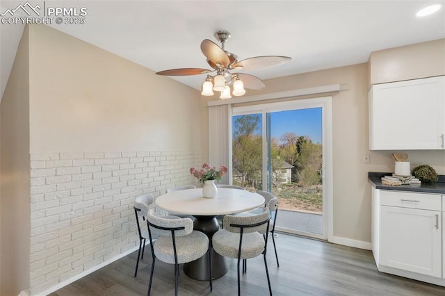 dining area featuring baseboards, wood finished floors, ceiling fan, and brick wall