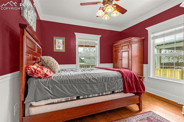 bedroom with wood finished floors, a wainscoted wall, ornamental molding, and ceiling fan