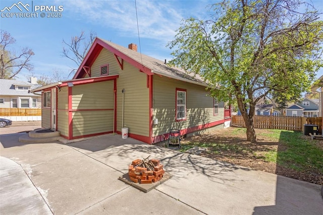 view of side of property with fence, a fire pit, central AC unit, and a patio