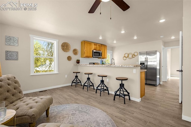 kitchen featuring a kitchen breakfast bar, a sink, stainless steel appliances, a peninsula, and a ceiling fan