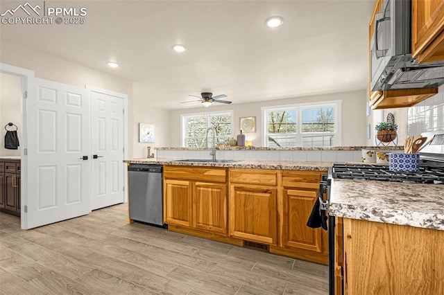 kitchen with brown cabinetry, appliances with stainless steel finishes, ceiling fan, a sink, and light wood-type flooring