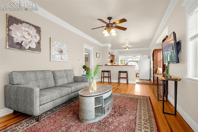 living room featuring ornamental molding, a ceiling fan, baseboards, and light wood-style floors