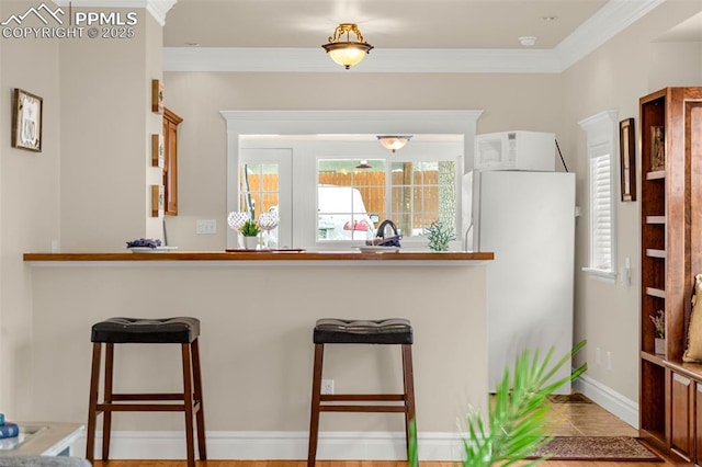kitchen featuring a kitchen breakfast bar, crown molding, baseboards, white appliances, and a peninsula
