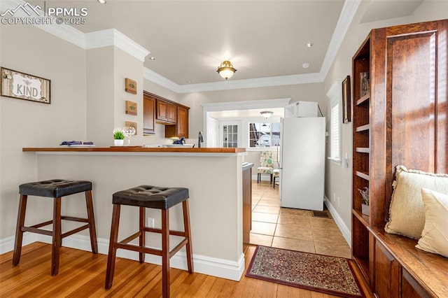 kitchen with a kitchen breakfast bar, crown molding, freestanding refrigerator, baseboards, and a peninsula