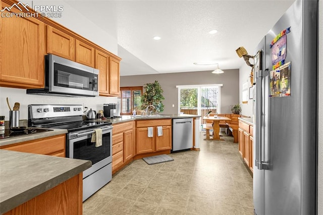 kitchen featuring a sink, brown cabinetry, a peninsula, appliances with stainless steel finishes, and recessed lighting