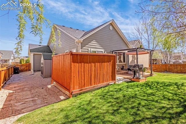 rear view of house with a fenced backyard, an outdoor structure, a lawn, a storage unit, and a deck