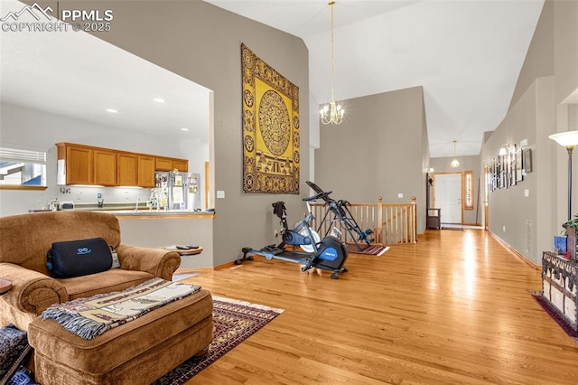 living area with a chandelier, light wood-type flooring, baseboards, and high vaulted ceiling