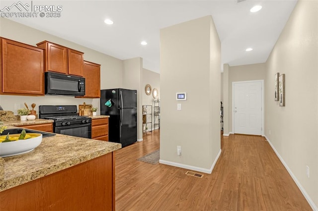 kitchen featuring light wood-type flooring, visible vents, brown cabinetry, light countertops, and black appliances
