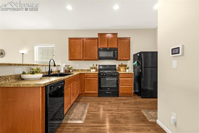 kitchen with a sink, black appliances, brown cabinets, light countertops, and dark wood-style flooring