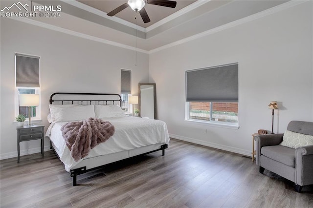 bedroom with crown molding, ceiling fan, a raised ceiling, baseboards, and wood finished floors
