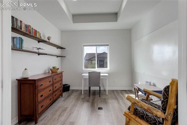 home office with baseboards, a raised ceiling, and light wood-style flooring