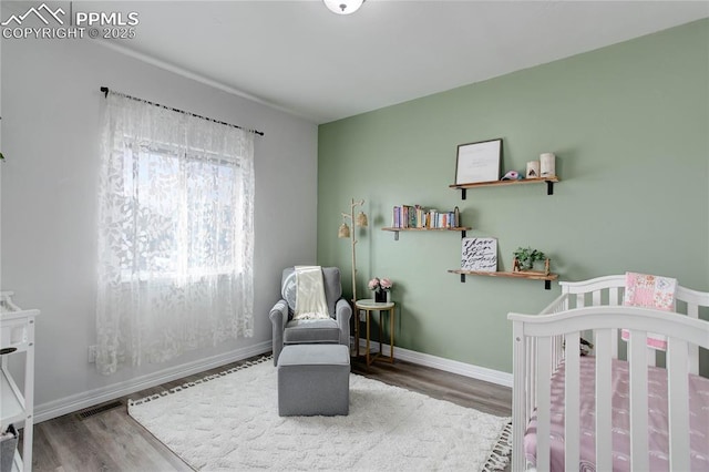 bedroom with baseboards, a crib, wood finished floors, and visible vents