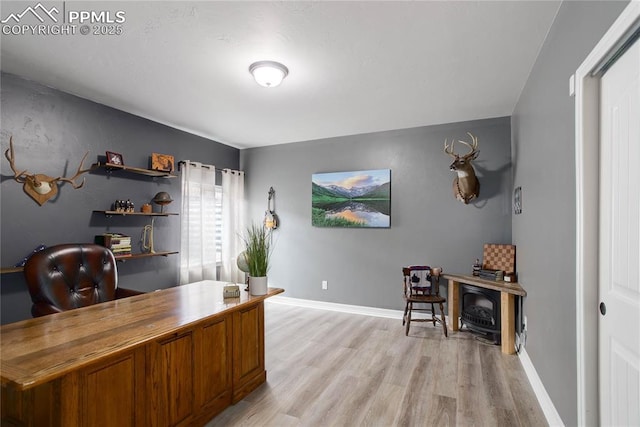 office space featuring light wood-style floors, a wood stove, and baseboards