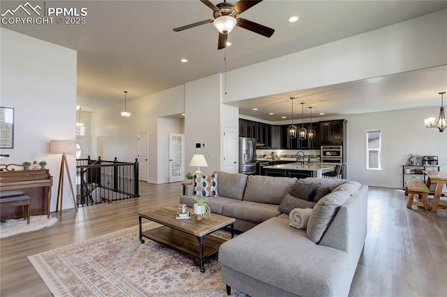 living area with light wood-style floors, recessed lighting, and ceiling fan with notable chandelier