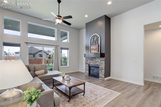 living room featuring visible vents, a fireplace, a high ceiling, a ceiling fan, and light wood-style flooring