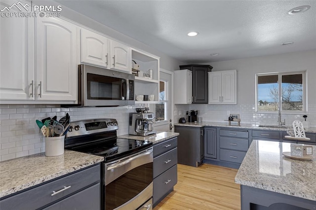 15930 Alta Plaza Cir, Peyton, CO 80831 - kitchen with appliances with stainless steel finishes, white cabinetry, light stone counters, decorative backsplash, and light wood finished floors