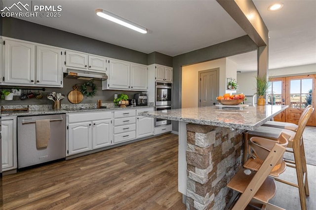 kitchen with light stone counters, a breakfast bar area, white cabinetry, stainless steel appliances, and under cabinet range hood