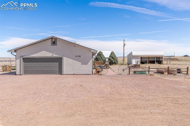exterior space with dirt driveway, a pole building, stucco siding, an outbuilding, and fence