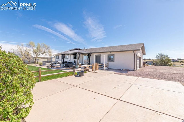 rear view of property featuring stucco siding, a gazebo, and an attached garage