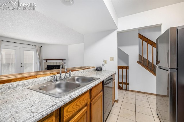kitchen with a sink, freestanding refrigerator, dishwashing machine, brown cabinets, and light countertops