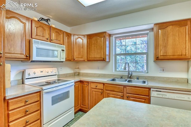 kitchen with tile patterned floors, a sink, brown cabinets, white appliances, and light countertops