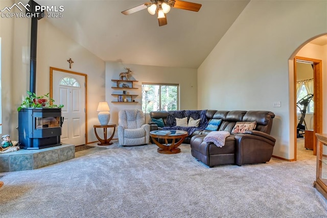carpeted living area featuring high vaulted ceiling, a ceiling fan, arched walkways, a wood stove, and baseboards
