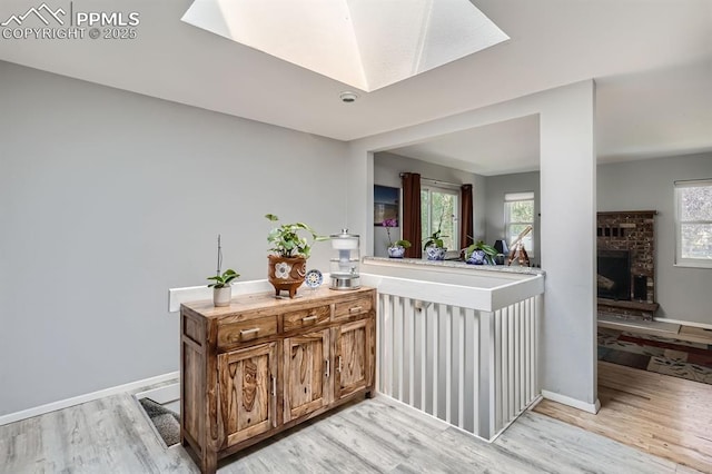bar featuring baseboards, a brick fireplace, a skylight, and light wood-style flooring