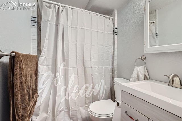 bathroom with a textured wall, vanity, curtained shower, and toilet