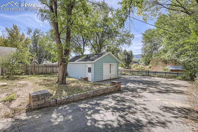 exterior space featuring a detached garage, a storage shed, aphalt driveway, fence, and an outbuilding