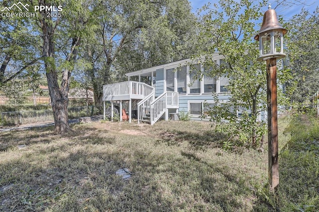 view of front of home with a wooden deck, a sunroom, stairway, and fence