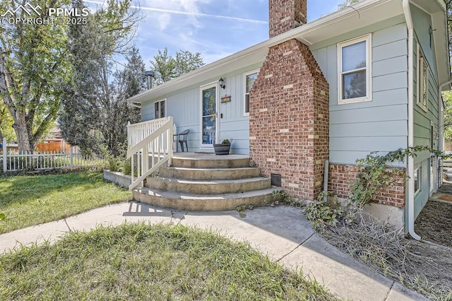 view of exterior entry with a chimney, fence, and a yard