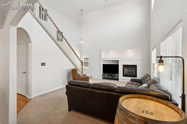 living room featuring baseboards, arched walkways, light colored carpet, and a towering ceiling