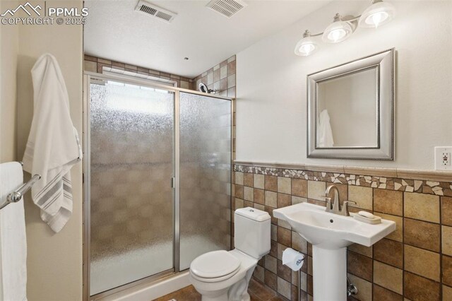full bathroom featuring visible vents, a shower stall, a wainscoted wall, and tile walls