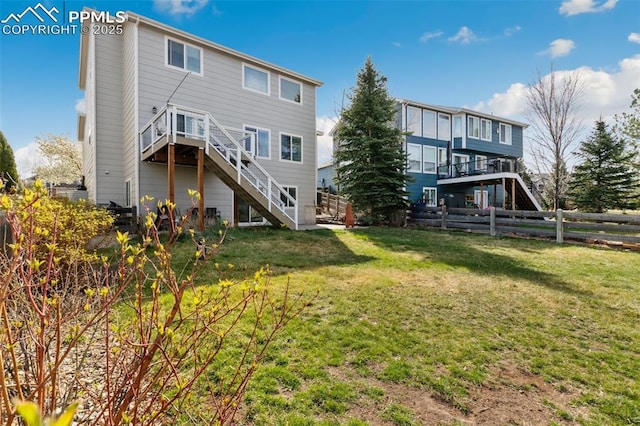 rear view of property with fence, a deck, a yard, and stairs