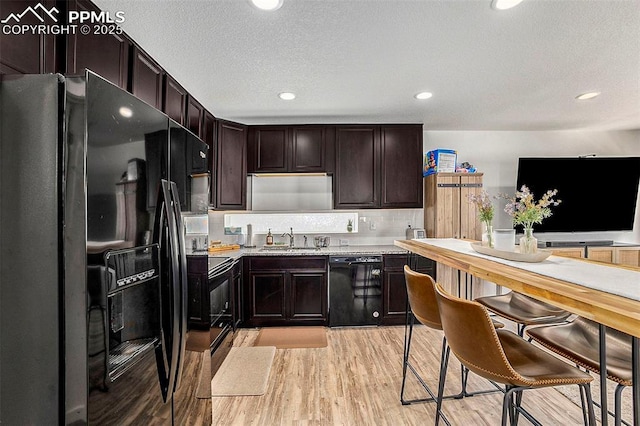 kitchen featuring light wood-style flooring, a sink, dark brown cabinets, light countertops, and black appliances