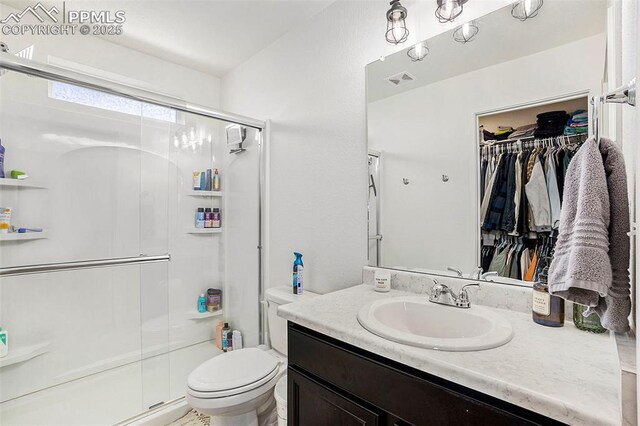 full bathroom with a shower stall, a spacious closet, visible vents, toilet, and vanity