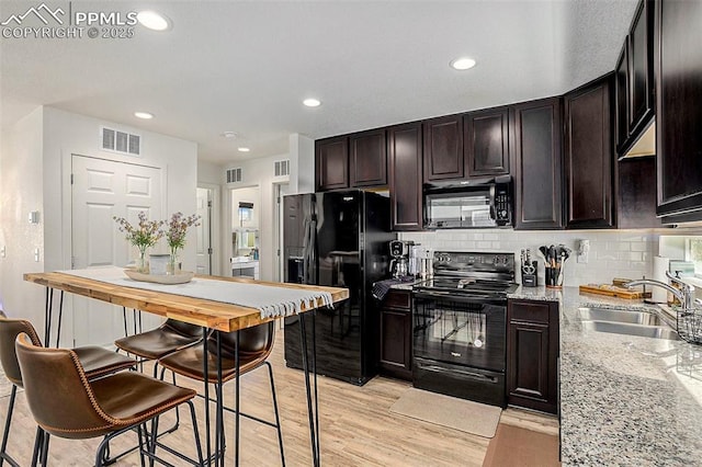 kitchen with a sink, visible vents, backsplash, light stone counters, and black appliances